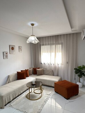 Una sala de estar moderna con un sofá, un reposapiés, una mesa de centro y una lámpara colgante.
