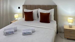 Ένα δωμάτιο ξενοδοχείου με ένα κρεβάτι, δύο φωτιστικά κομοδίνου, ένα κρεμαστό φωτιστικό, ένα προσκέφαλο και δύο φωτογραφίες σε κ ορνίζες στον τοίχο.