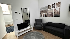 A living room with a flat-screen TV, a grey armchair, a black sofa, and a wall with cityscape photographs. - Trendsetter Retreat in Fashion Hub (Antwerp)