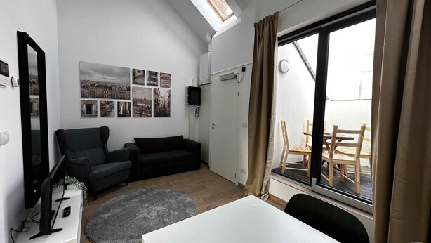 A compact living space with a sofa, a TV, a dining table, and a large window with curtains. - Trendsetter Retreat in Fashion Hub (Antwerp)