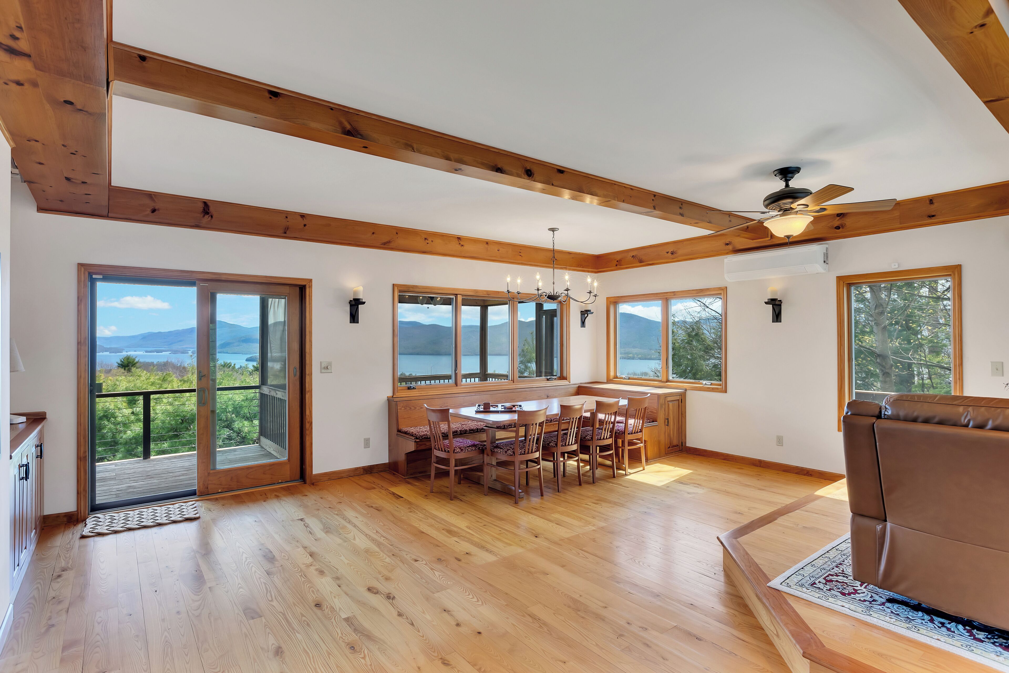 Amplia habitación con pisos de madera, zona de comedor con sillas, sofá y ventanas amplias con vista a las montañas.