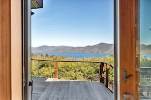 Una terraza de madera con barandilla metálica que da a un paisaje montañoso y una masa de agua.