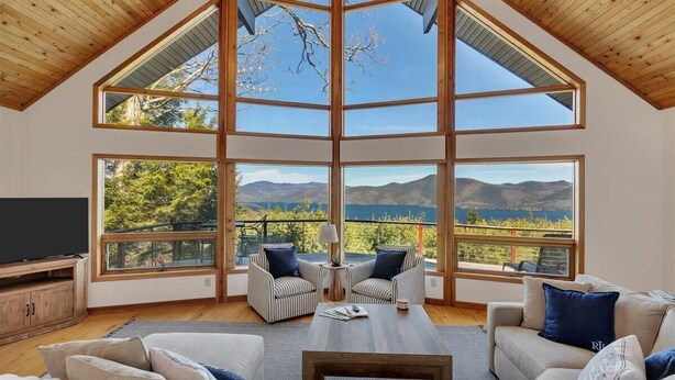 A spacious living room with a high ceiling, large windows, and a view of mountains and a lake. - Luxury Retreat w Gorgeous Lake Views, Minutes to Marina, Beach & Dining (Diamond Point)