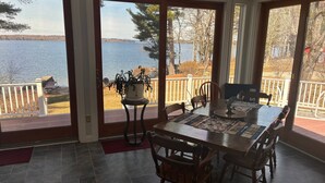 A dining area with a table and chairs, a potted plant, and a view of a lake through large glass doors. - Spacious 5-bedroom lake house in Standish, ME (Standish)