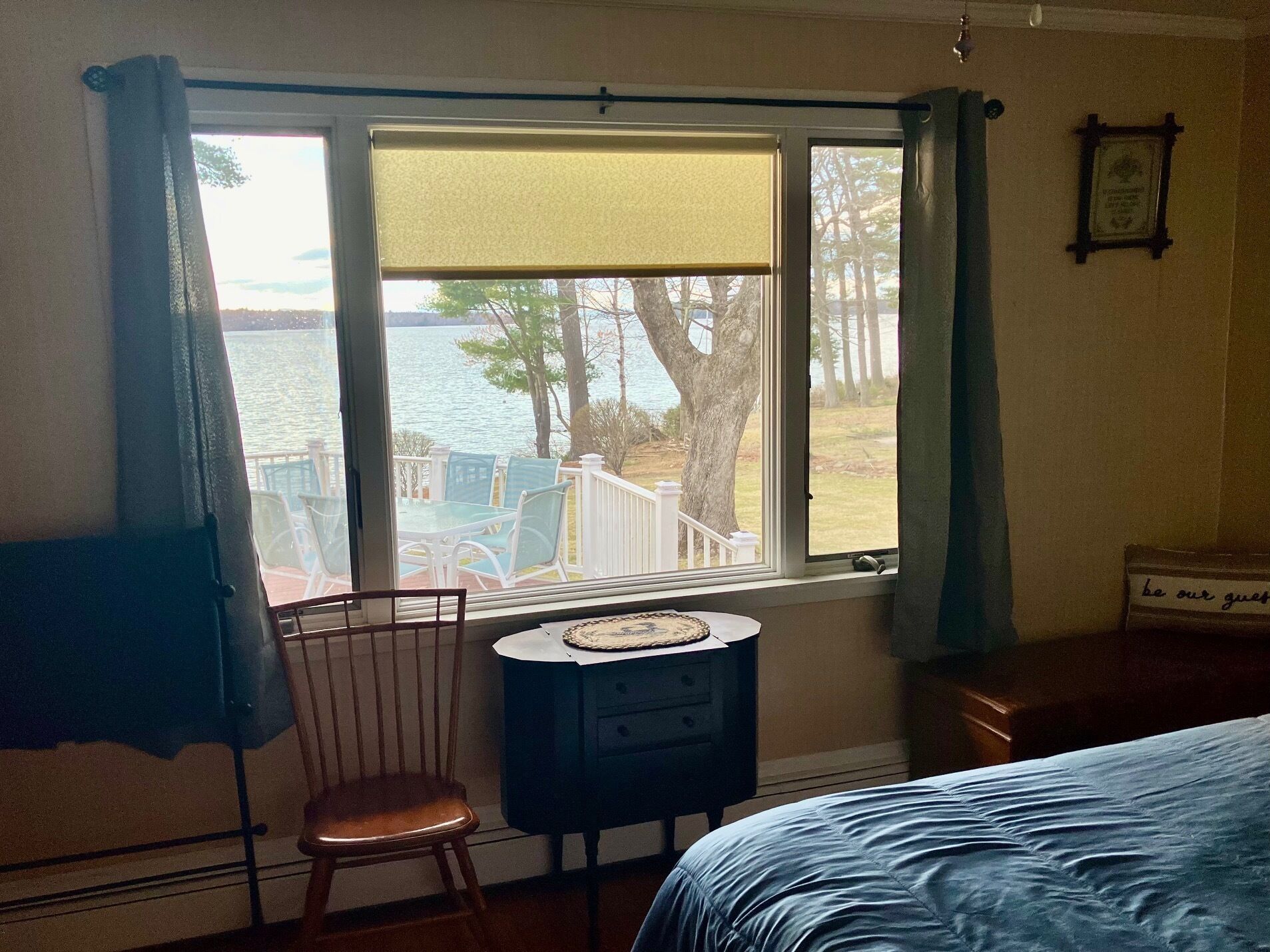 A bedroom with a view of a lake, a chair, a small table, and a bed.