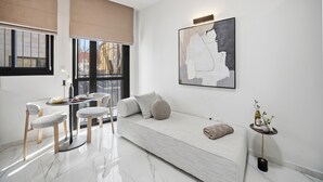 Un salon moderne comprenant un canapé, une table à manger avec des chaises, un grand tableau abstrait et une petite table d’appoint avec un vase.