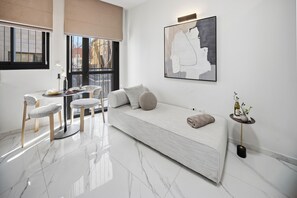 A modern living room with a sofa, a dining table with chairs, a large abstract painting, and a small side table with a vase. - Design Apartment - Heart of Mahane Yehuda - (JERUSALEM)
