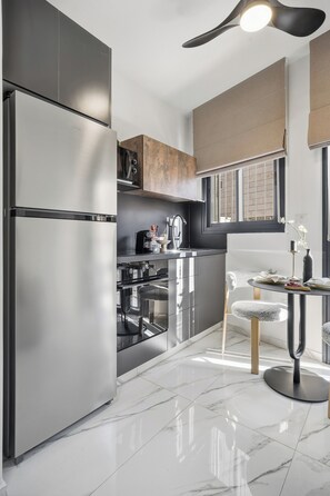 A modern kitchen with stainless steel appliances, a dining area with a round table and chairs, and a large window providing natural light. - Design Apartment - Heart of Mahane Yehuda - (JERUSALEM)