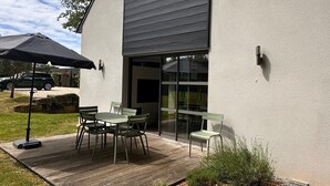 En moderne bygning med fladt tag, en terrasse med udendørs møbler og en klar himmel.