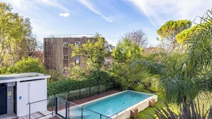 A swimming pool with a wooden deck, surrounded by greenery and a building in the background. - Spacious Apartment a/c 1br/4p - With Pool (Cannes)