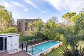 A swimming pool with a wooden deck, surrounded by greenery and a building in the background. - Spacious Apartment a/c 1br/4p - With Pool (Cannes)