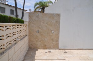 Un espace de douche extérieur privatif, doté d’un mur en marbre, d’une clôture décorative et d’un sol carrelé.