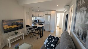 Una cocina moderna con armarios blancos, un refrigerador y un microondas. Hay una zona de comedor con una mesa y sillas.