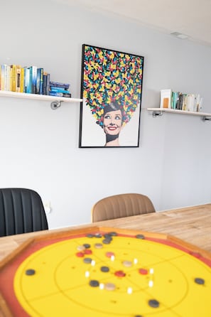 A room with a wooden table, chairs, a bookshelf, and a framed artwork on the wall.