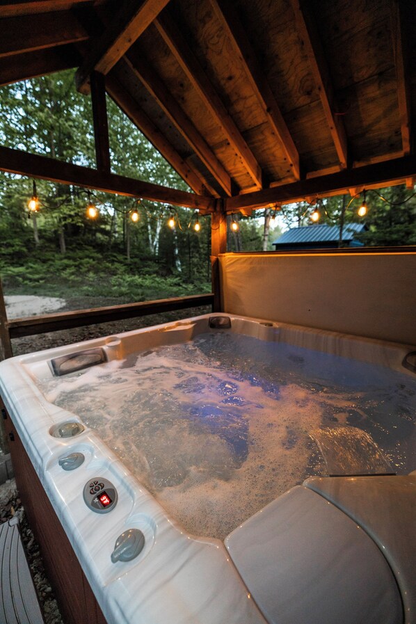 A hot tub with controls, surrounded by wooden beams and a view of a forested area.