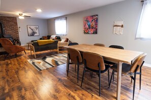 A modern living room with a wooden dining table, comfortable seating, a fireplace, and decorative wall art.