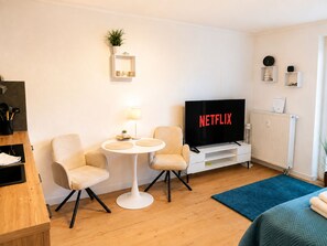 A modern living room with a television, two chairs, a small table, a lamp, and a blue rug. - Vellmar Oase at Ahnepark with a terrace—quiet—24/7 self-check-in (Vellmar)