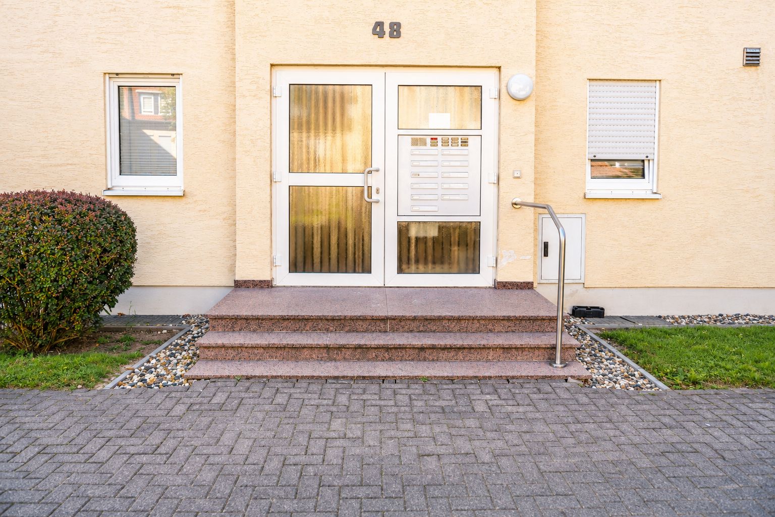 Ein Gebäude mit einer Doppeltür, einem kleinen Fenster und der Hausnummer 48 an der Wand.
