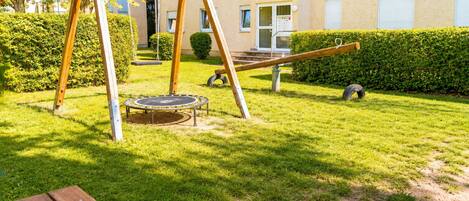 A playground with a swing set and a trampoline in a grassy area with a building in the background.