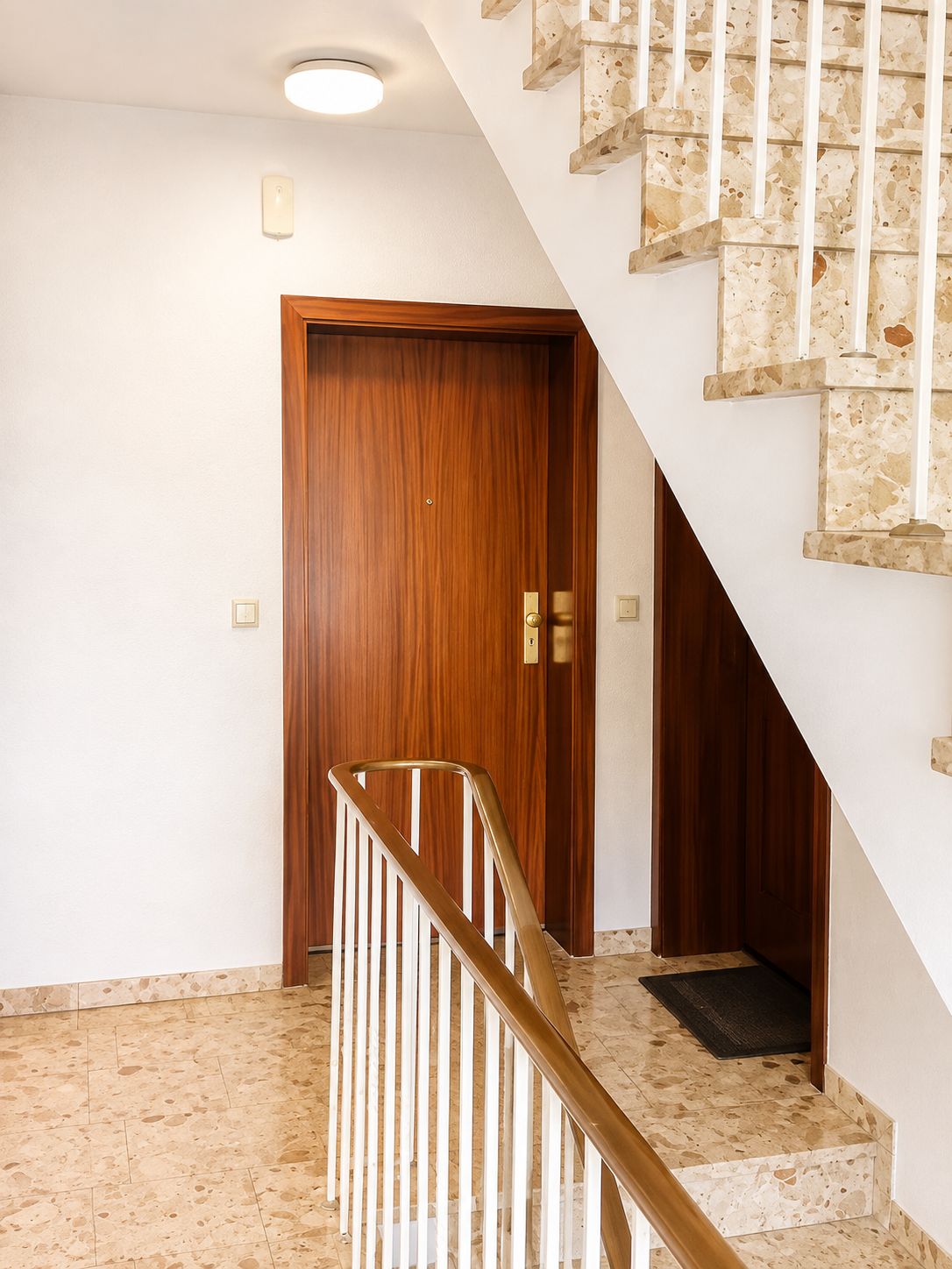 Eine Treppe mit einem hölzernen Geländer und einer Tür am Fuß.