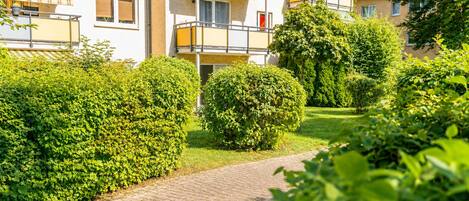A residential building with multiple balconies, a paved pathway, and well-maintained greenery.