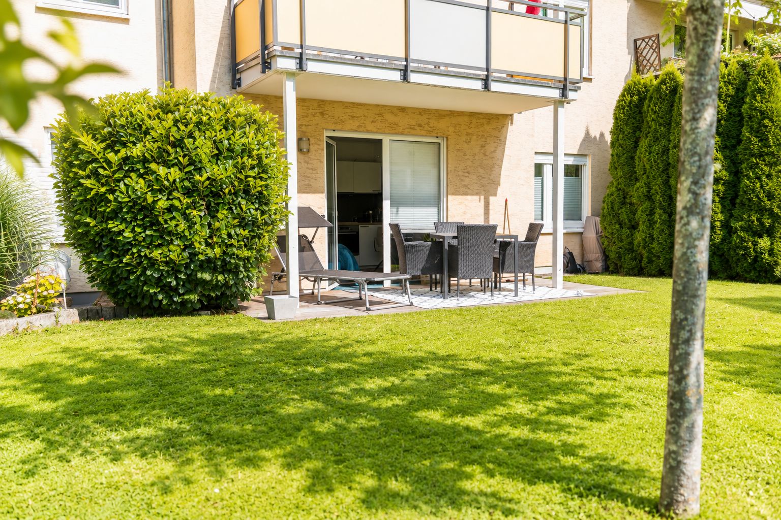 A residential building with a balcony, a patio with outdoor furniture, and a well-maintained lawn.