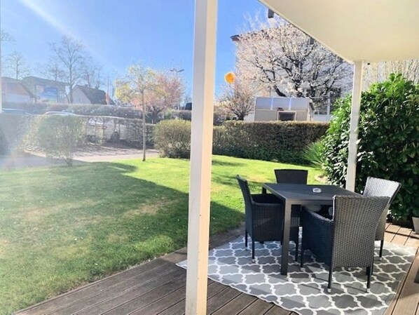 Une terrasse couverte avec une table et des chaises, un tapis à motifs et une vue sur un jardin et des arbres.