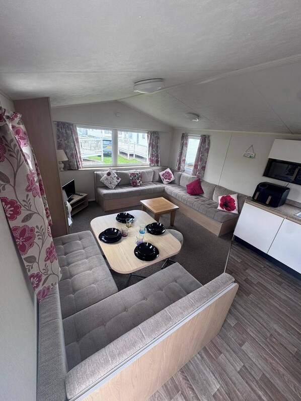 A compact living space with a sofa, a dining table with plates, a TV, and a view of the outside.