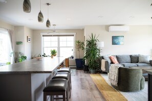A modern kitchen with a central island, bar stools, a dining table, and a large window.
