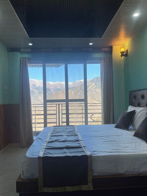 A bedroom with a bed, a view of mountains, and a balcony.