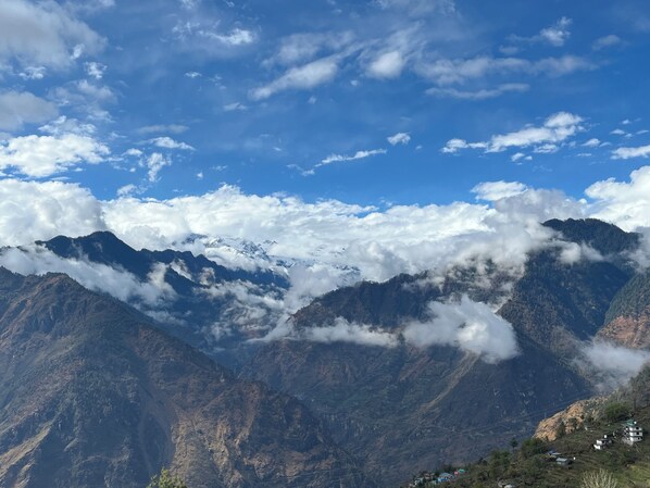 A mountainous landscape with snow-capped peaks, a clear sky, and a valley with scattered houses.