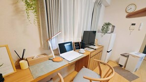 Ein kleines Zimmer mit Schreibtisch, Laptop, Stuhl und kleinem Kühlschrank.
