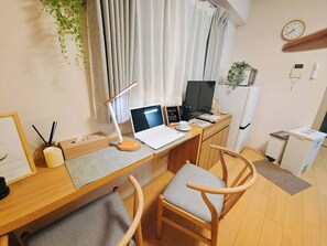 Ein kleines Zimmer mit Schreibtisch, Laptop, Stuhl und kleinem Kühlschrank.