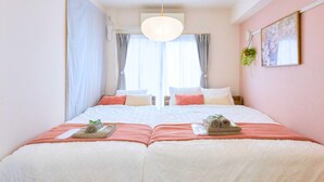 Ein Doppelbett mit weißer und pfirsichfarbener Bettdecke, eine hängende Pflanze und ein Bild an der Wand.