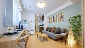 Ein modernes Wohnzimmer mit einer Couch, einem Couchtisch, einem Esstisch und Stühlen. Im Hintergrund ist eine Küche erkennbar.