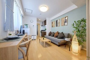 Ein modernes Wohnzimmer mit einer Couch, einem Couchtisch, einem Esstisch und Stühlen. Im Hintergrund ist eine Küche erkennbar.