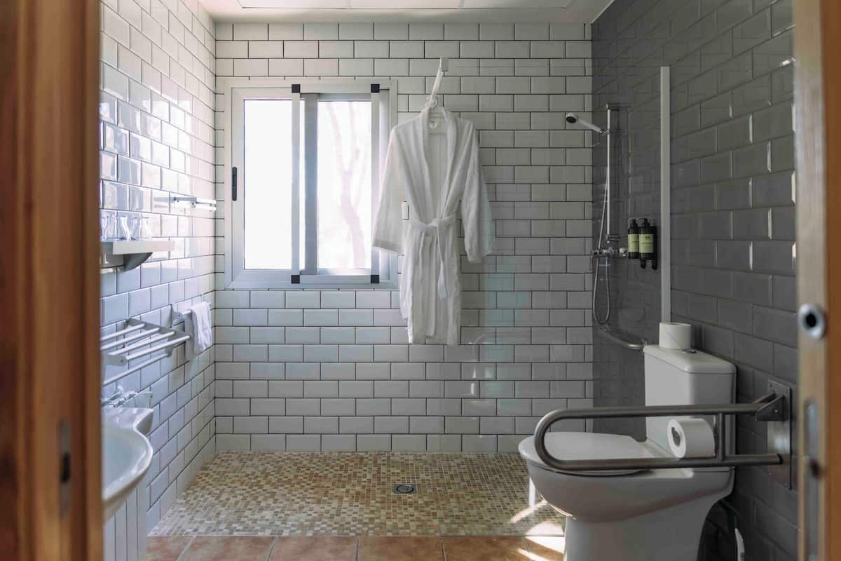A bathroom with white tiled walls, a shower, a toilet, and a window.