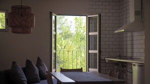 Eine moderne Küche mit Essbereich, einer Couch mit Kissen und Blick durch eine offene Tür auf Grünflächen.