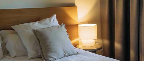 Una cama bien hecha con sábanas y almohadas blancas, una lámpara de noche y un cabecero de madera.