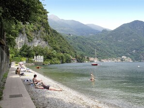 A lakeside beach with people sunbathing and swimming, surrounded by mountains and a small town. - Casa Fujada by Interhome (Menaggio)
