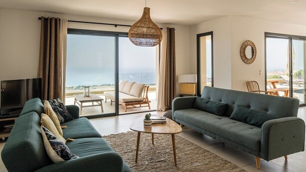A modern living room with a sofa, a coffee table, a TV, and a large window with a view. - Villa Wonderfull sea view (Sari-Solenzara)