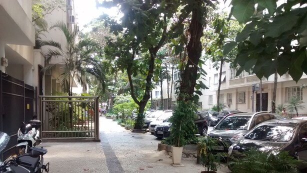 Ein gepflasterter Weg, gesäumt von parkenden Autos und Kübelpflanzen, führt zu einem verschlossenen Eingang.