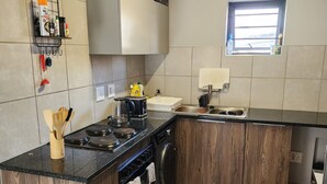 Une cuisine moderne dotée d’une cuisinière, d’un four et d’un lave-vaisselle encastrés, de meubles de rangement en bois et d’une petite fenêtre.