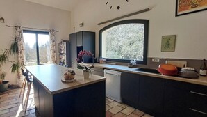 Een moderne keuken met een centraal eiland, een vaatwasser en een groot raam met uitzicht op bomen.