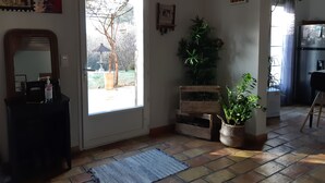 Een kamer met een groot raam, een spiegel, een houten bankje, een potplant en een betegelde vloer.
