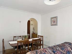 A room with a dining table, chairs, a bed, a framed picture, and a doorway. - Salceda Apartment - 6901 (Noja)