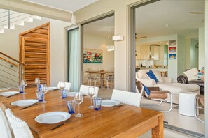Ein Essbereich mit Holztisch, gedeckt für vier Personen, eine Treppe und ein Wohnzimmer mit Sofa und Couchtisch.