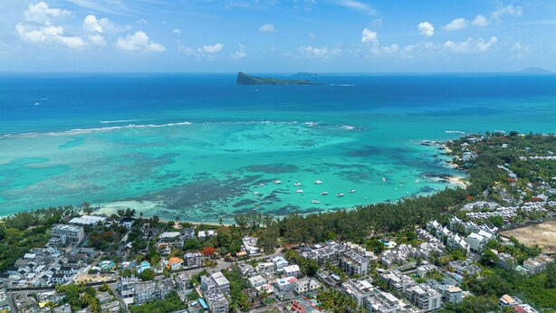 An aerial view of a coastal town with a marina, residential buildings, and a distant island. - Element penthouse with private pool near the beach (Cap Malheureux)