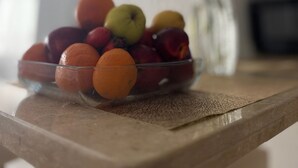 Eine Schale mit Obst auf einem Tisch, im Hintergrund eine Blumenvase.