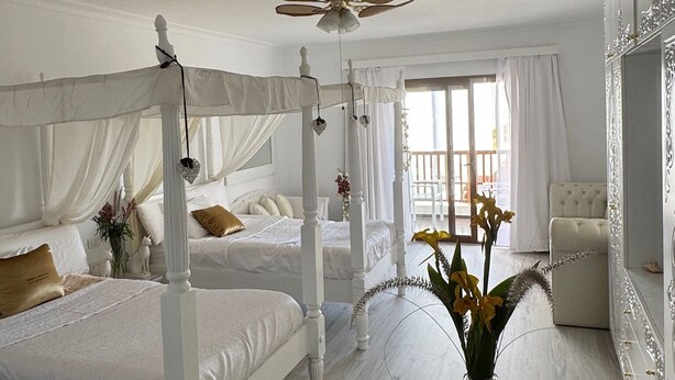 Ein Himmelsbett mit Baldachin, ein Deckenventilator und eine Obstschale auf einem Tisch.